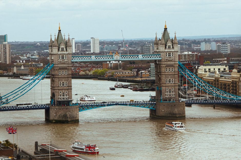 Photograph of Tower Bridge in London showing the two iconic Gothic-style towers with decorative spires and intricate stonework, connected by a high-level walkways and a bascule section in the middle. 