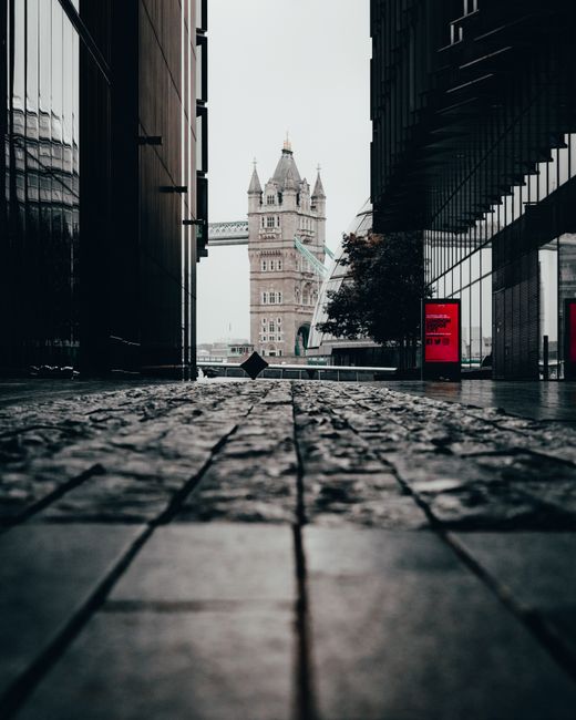 Photograph of Tower Bridge in London showing the two iconic Gothic-style towers with decorative spires and intricate stonework, connected by a high-level walkways and a bascule section in the middle. 